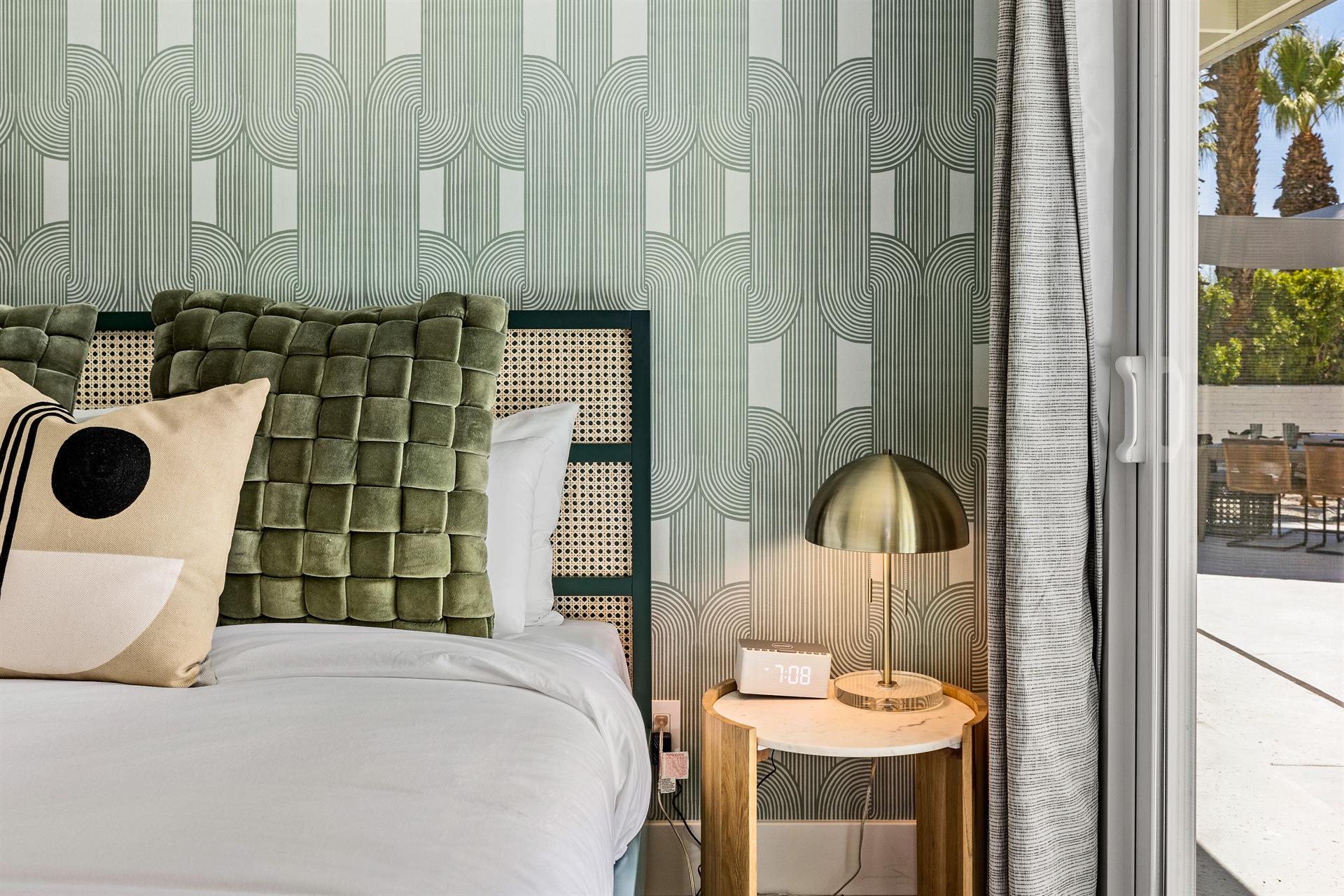 Bedroom with green velvet headboard, patterned wallpaper and brass lamp